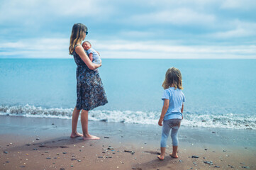 Young mother standing by the sea with her baby and preschooler