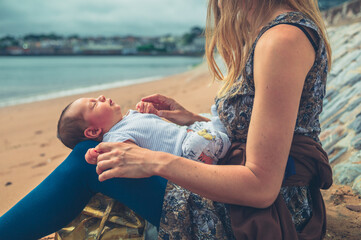 Fototapeta na wymiar Young mother sitting on the beach with her newborn baby