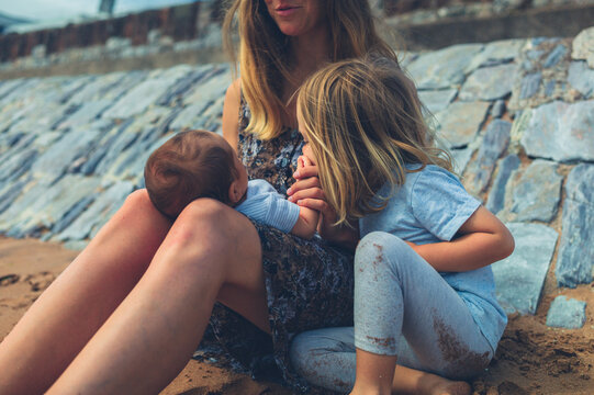 Young mother sitting on the beach with her preschooler and newborn baby