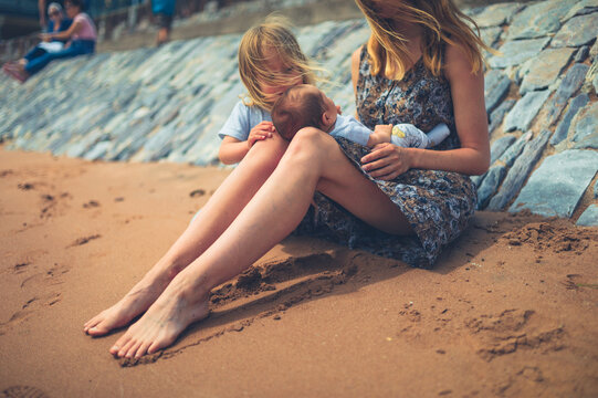 Young mother sitting on the beach with her preschooler and newborn baby