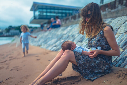 Young mother sitting on the beach with her newborn baby