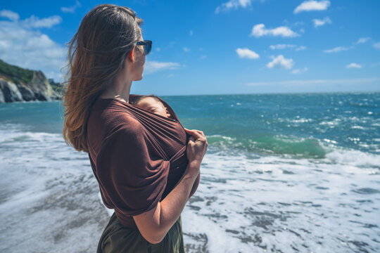 Young mother standing on the beach with baby in sling