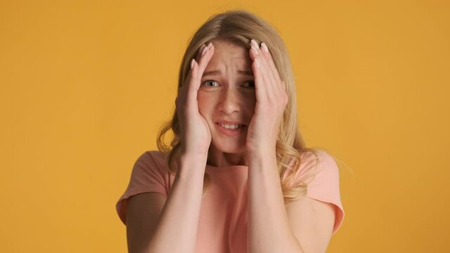 Beautiful afraid blond girl scaredly closing face with hands over colorful background. Fear expression