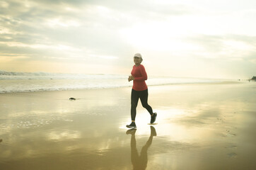 Silhouette of middle aged woman running on the beach - 40s or 50s attractive mature lady doing jogging workout enjoying fitness and healthy lifestyle at beautiful sea sunset