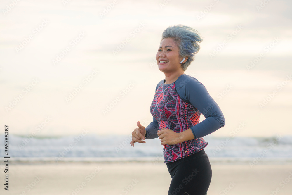 Wall mural fit and happy middle aged woman running on the beach - 40s or 50s attractive mature lady with grey h