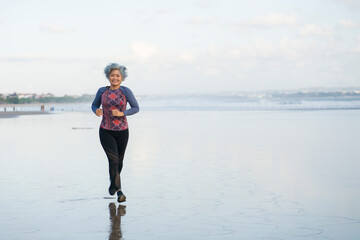 fit and happy middle aged woman running on the beach - 40s or 50s attractive mature lady with grey hair doing jogging workout enjoying fitness and healthy lifestyle