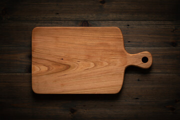 Hand-made cherry wood cutting board on the darkened wooden tabletop - obrazy, fototapety, plakaty