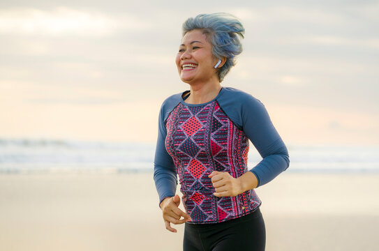 Fit And Happy Middle Aged Woman Running On The Beach - 40s Or 50s Attractive Mature Lady With Grey Hair Doing Jogging Workout Enjoying Fitness And Healthy Lifestyle