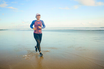 fit and happy middle aged woman running on the beach - 40s or 50s attractive mature lady with grey hair doing jogging workout enjoying fitness and healthy lifestyle