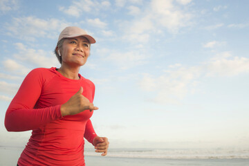 fit and happy middle aged woman running on the beach - 40s or 50s attractive mature lady with grey hair doing jogging workout enjoying fitness and healthy lifestyle