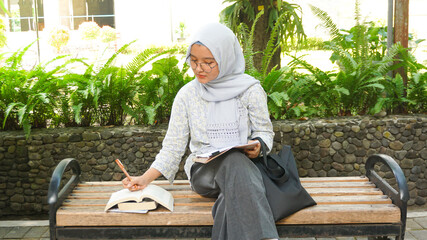 Asian hijab girl is writing notes in the campus garden
