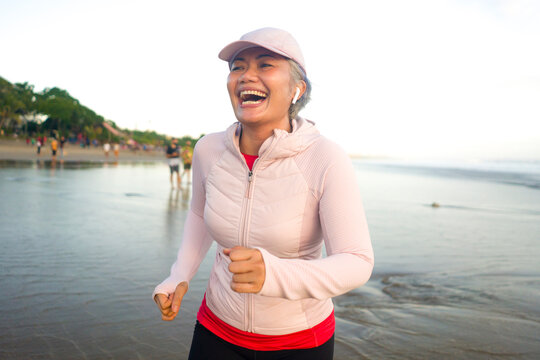 fit and happy middle aged woman running on the beach - 40s or 50s attractive mature lady with grey hair doing jogging workout enjoying fitness and healthy lifestyle