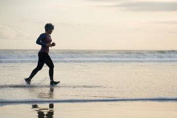 Silhouette of middle aged woman running on the beach - 40s or 50s attractive mature lady doing...