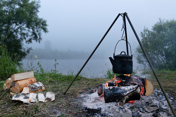 the kettle is heated on the fire in the evening. Tourist camping by the river. travel to Siberia....