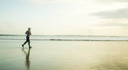 Silhouette of middle aged woman running on the beach - 40s or 50s attractive mature lady doing jogging workout enjoying fitness and healthy lifestyle at beautiful sea sunset