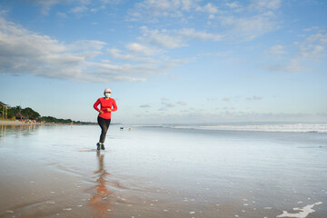 new normal running workout with face mask - attractive and happy middle aged woman on her 40s or 50s doing post quarantine jogging at beautiful beach in healthy lifestyle