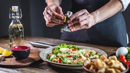 Chef is grating the cheese into an appetizing fresh salad. Concept of cooking delicious Caesar
