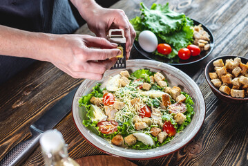 Chef is grating the cheese into an appetizing fresh salad. Concept of cooking delicious Caesar