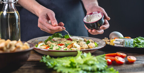 Chef is dressing the Caesar salad with a special fresh sauce. Concept of the process of cooking a delicious dish