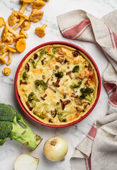 Homemade lorraine quiche or pie with chicken, broccoli and chanterelles in red uniform on a marble table. Tart with meat and mushrooms. Top view