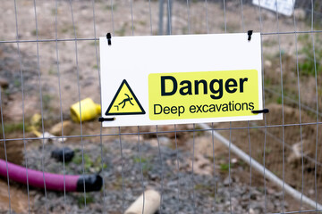Deep excavations danger sign on fence with trench hole in background on construction site