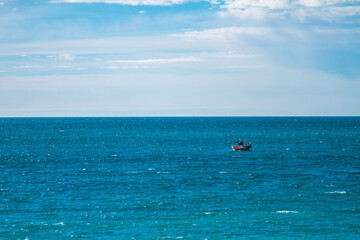 Small ship sailing on the horizon in a waving sea and cloudy sky.