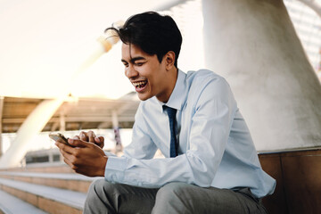 Smiling Young Asian Businessman Using Mobile Phone in the City. Sitting at the Staircase