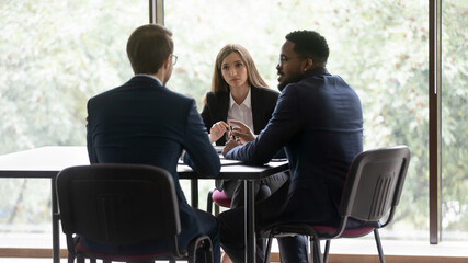 Rear view African Caucasian businessmen in suits sit at desk with European businesswoman, involved...
