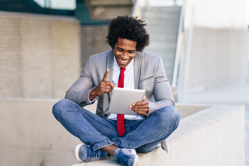 Black Businessman using a digital tablet sitting near an office building.