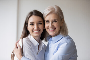 Head shot portrait mature mother cuddles grown-up daughter. Different generation relatives women posing smile for camera. Unconditional love and cherish. Understanding adult kid warm relations concept