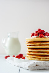 Delicious homemade golden pancakes with fresh berries and milk on a light backgrouns.