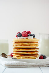 Delicious homemade golden pancakes with fresh berries and milk on a light backgrouns.