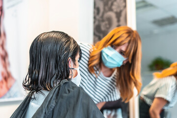 Hairdresser with face mask cutting hair to client. Safety measures for hairdressers in the Covid-19 pandemic. New normal, coronavirus, social distance