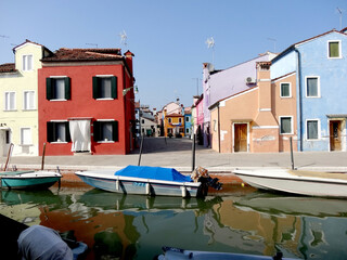 colorful houses and boats with reflections in the canal on the island of Burano in Venice