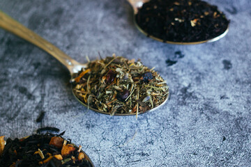 Fototapeta na wymiar Various types of herbal tea in spoons. Spoons with dry tea leaves. Tea on a concrete background