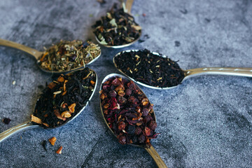 Various types of herbal tea in spoons. Spoons with dry tea leaves. Tea on a concrete background