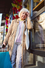 Fototapeta na wymiar Tired old age female wearing coat with multicolor shopping bags