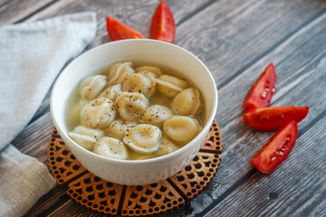 Dumplings with broth in a plate. Traditional Russian dish. Pelmeni with tomatoes on a wooden table