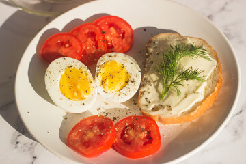 Delicious breakfast on the table. Boiled eggs, tomatoes, cream cheese sandwich, dill on a plate