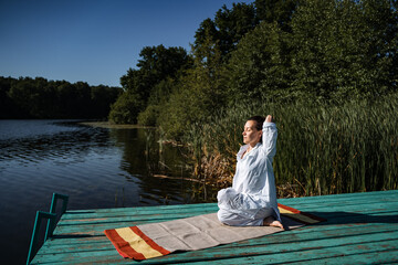 a young girl does yoga on a lake on a Sunny summer day, meditation, relaxing pose, solitude in nature, peace, relaxation, asana, healthy lifestyle, life style, Zen