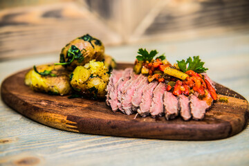Grilled meat slices and potatoes with fresh vegetables served on wood plate. The food in the restaurant. Food styling and restaurant meal serving.