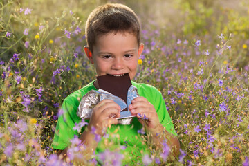 happy boy biting chocolate surrounded by wildflowers concept