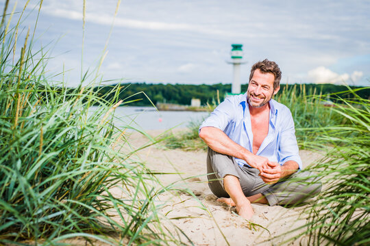 bestager Mann sitzt am strand und lächelt in sich hinein mit viel platz drumherum  