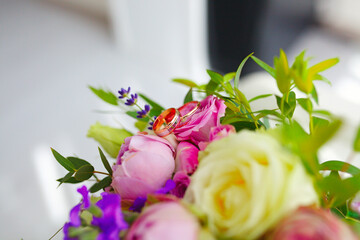 Close up of golden wedding rings of young and fresh flower bouquet of roses and other blooming beautiful flowers