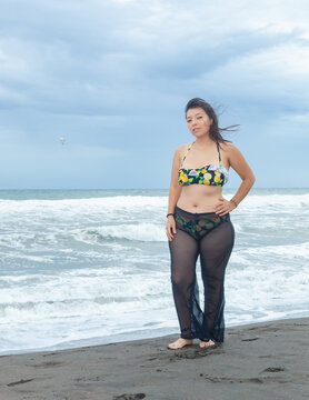 Muchacha en la playa con traje de ba&ntilde;o, mar con olas al fondo, cielo noblado.