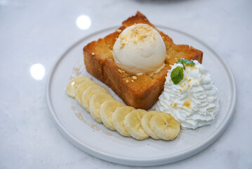 Honey Toast, a square toast baking with butter and topped with vanilla ice cream and honey sauce served with banana and whip cream. Top view.