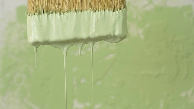 Thick green colour paint drop falls slowly freshly painted surface background. Slow motion artistic footage, paint pours from wide brush paper, plate, or table. Art house industrial decor concept
