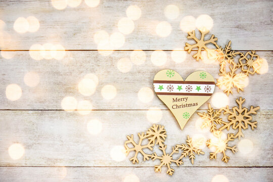 Christmas toys, heart with inscription "Merry Christmas" and wooden snowflakes, on old wooden background. Winter concept, new year decorations. Flat lay, top view, copy space. Selective focus