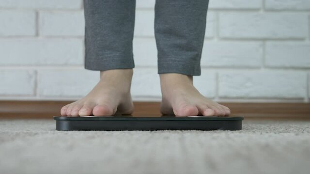 Girl measure her weight. The teenager's feet are on the scales.