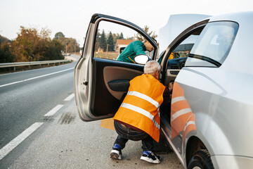 Two road assistant workers in towing service trying to start car engine with jump starter and energy station with air compressor. Roadside assistance concept.